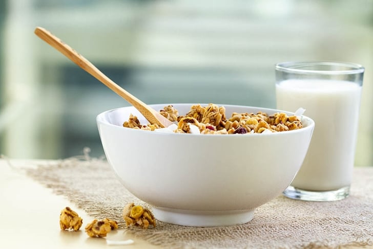 Dry breakfast cereals. Crunchy honey granola bowl with flax seeds, cranberries and coconut and a glass of milk on a table. Healthy and fiber food. Breakfast time