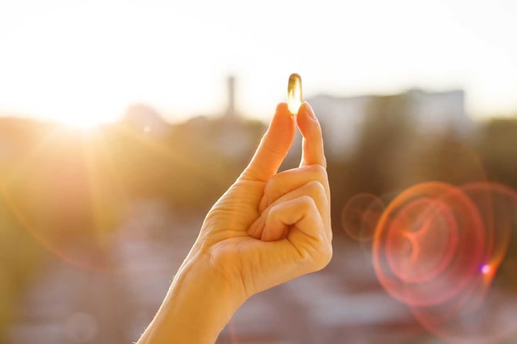 Hand of a woman holding fish oil Omega-3 capsules, urban sunset background. Healthy eating, medicine, health care, food supplements and people concept