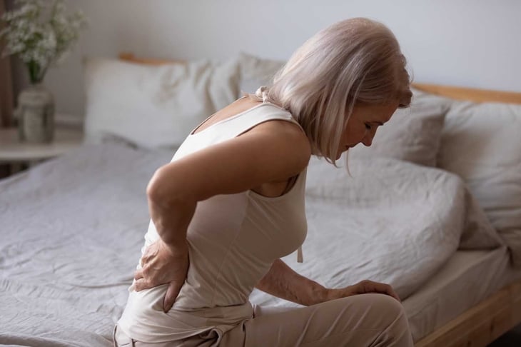 Upset mature woman suffering from backache after sleep, rubbing stiff muscles, unhappy older female sitting on bed at home, feeling discomfort, because of bad posture or uncomfortable bed