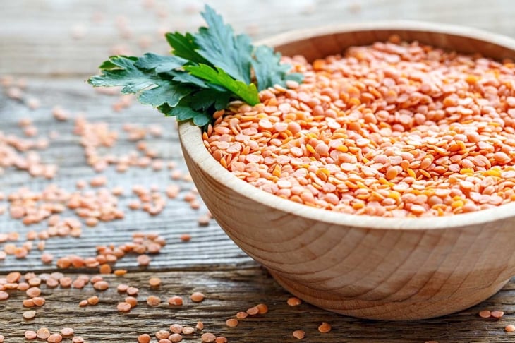 Heap of red lentils and parsley in a bowl on old wooden table.