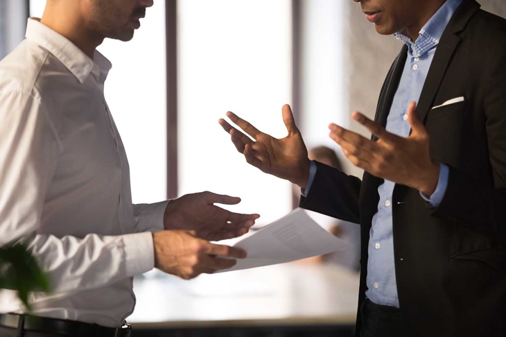 Close up executive manager dissatisfied by African American employee work results, holding financial report with stats, colleagues arguing, discussing business failure, partners disputing at work