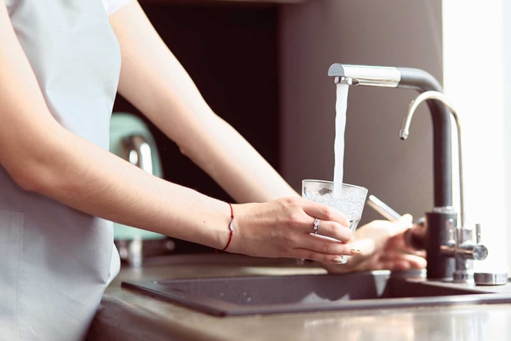 Human hand holding glass pouring fresh drink water at kitchen faucet