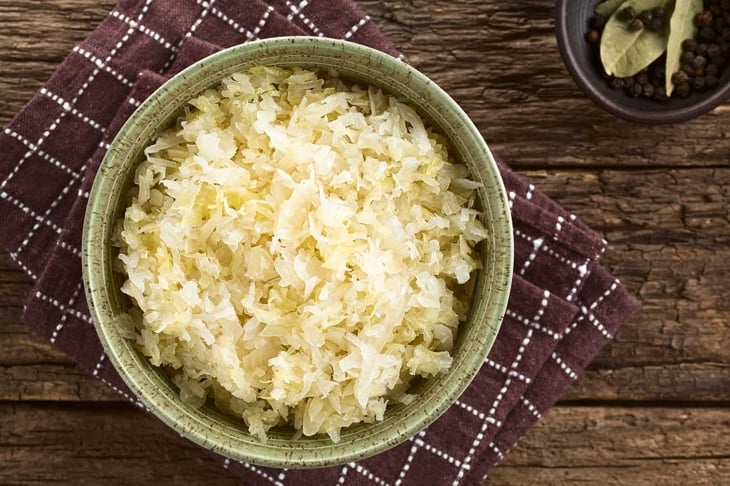 Fresh healthy sauerkraut in bowl with black pepper and bay leaves on the side, photographed overhead on rustic wood (Selective Focus, Focus on the sauerkraut)