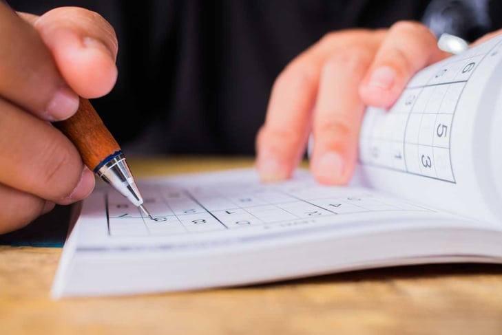 Student is trying solve sudoku with color pencil as hobby at outdoor. Sudoku originally called Number Place logic-based, number-placement puzzle for Learning.