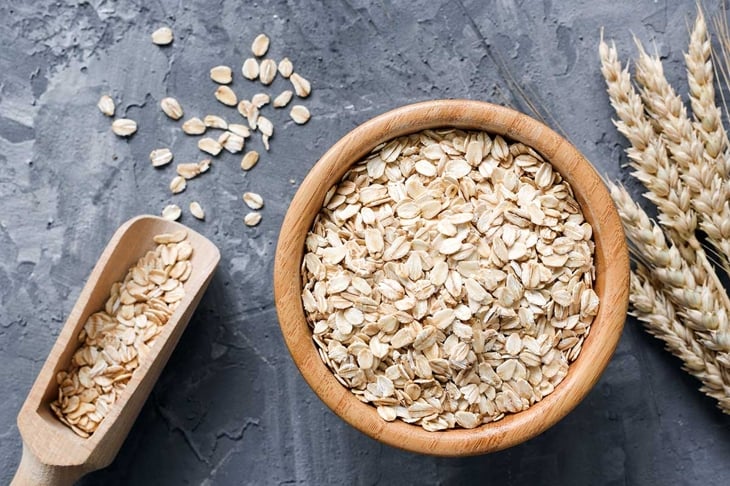 Rolled oats or oat flakes in wooden bowl and golden wheat ears on stone background. Top view, horizontal. Healthy lifestyle, healthy eating, vegan food concept