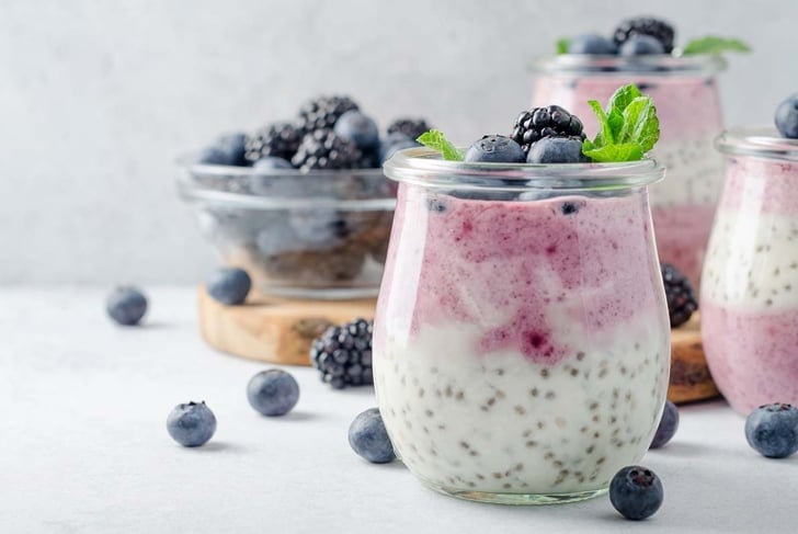 Acai berry and chia seed pudding with blueberries and blackberries in glass jars on a light white table. Copy space, horizontal image, front view