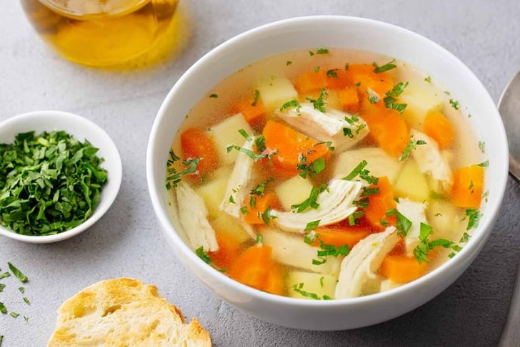 Chicken soup with vegetables in white bowl. Grey stone background. Close up.