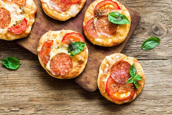 Mini Pizzas - Fresh homemade mini pizzas with pepperoni, cheese, tomatoes and basil on rustic wooden background with copy space.